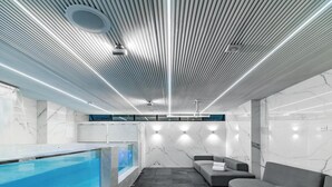 A modern indoor swimming pool with a tiled floor, a built-in bench, and a seating area with a sofa. - 444 jds (Medellín)
