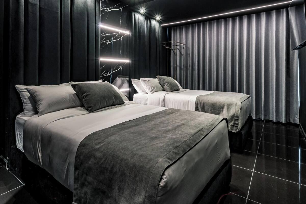 Una habitación de hotel moderna con una cama grande, dos camas más pequeñas, un armario y un espejo.