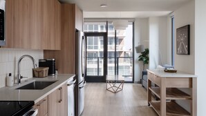 A modern kitchen with wooden cabinets, stainless steel appliances, a large window, and a view of the city. - Kasa at The Waller Austin (Austin)