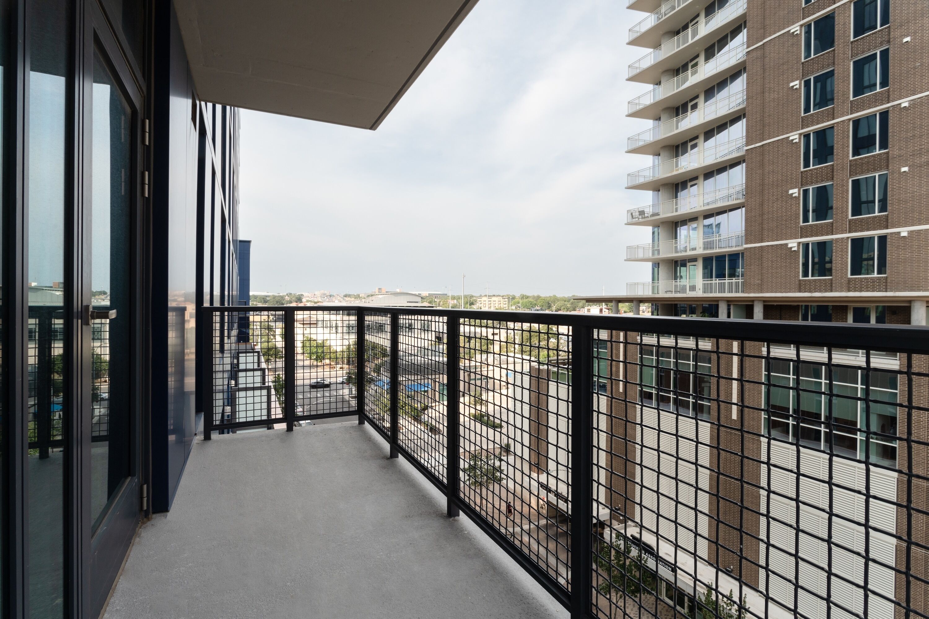 A balcony with a metal railing, a clear view of a parking lot, and a building with multiple floors and balconies in the background.