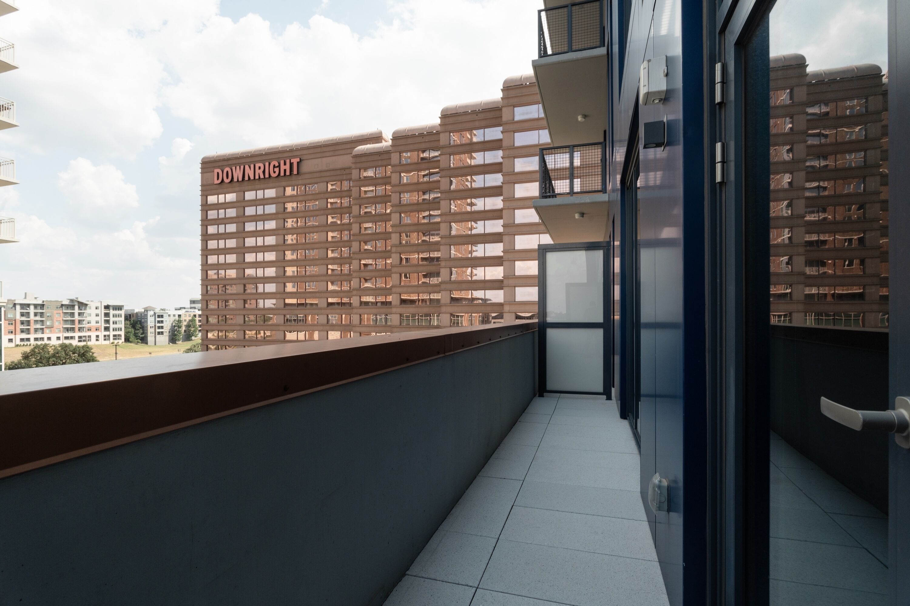 A modern building with a 'DOWNRIGHT' sign, a balcony with a glass door, and a view of other buildings.