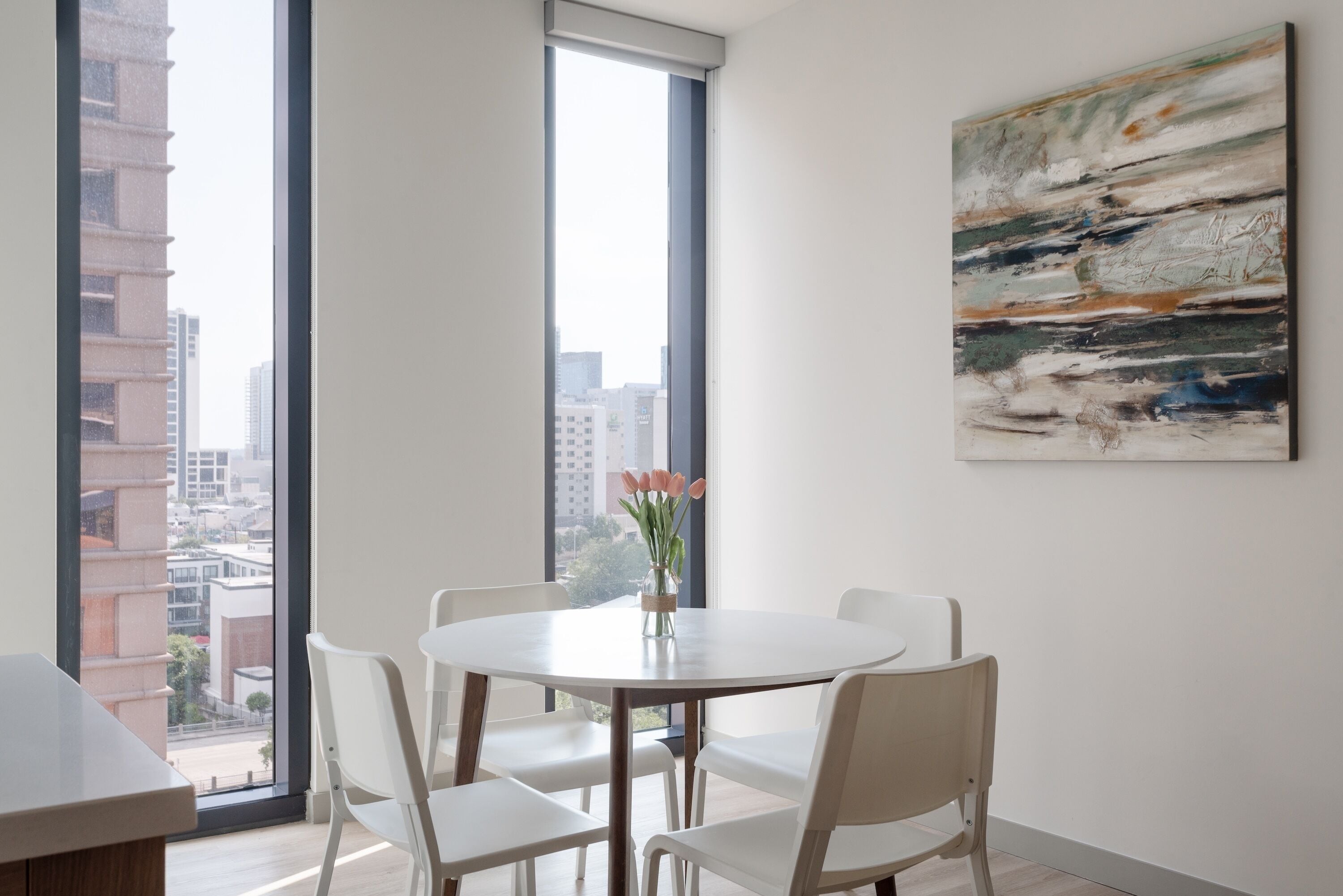Een moderne eetruimte met een ronde tafel, witte stoelen en een vaas met bloemen.