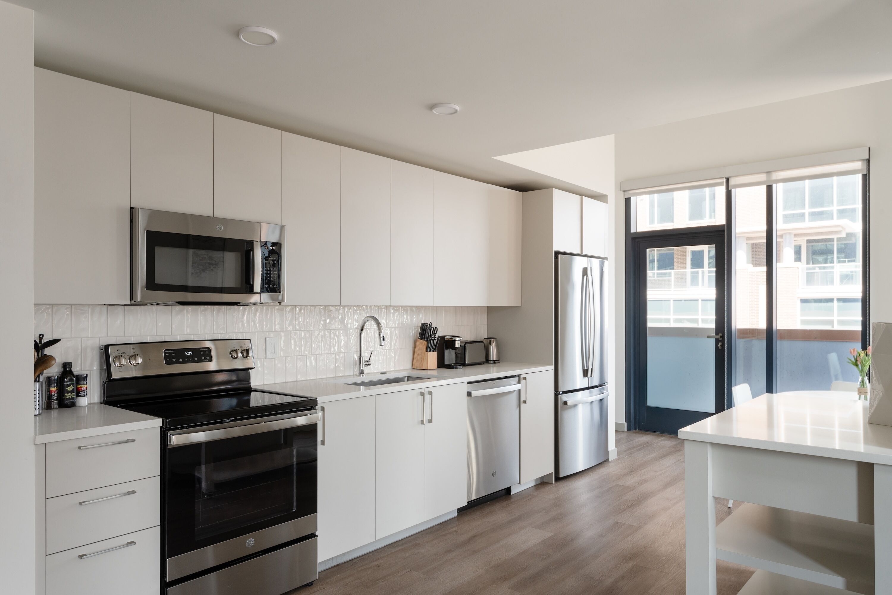 A modern kitchen with white cabinetry, stainless steel appliances, and a view to the outside.