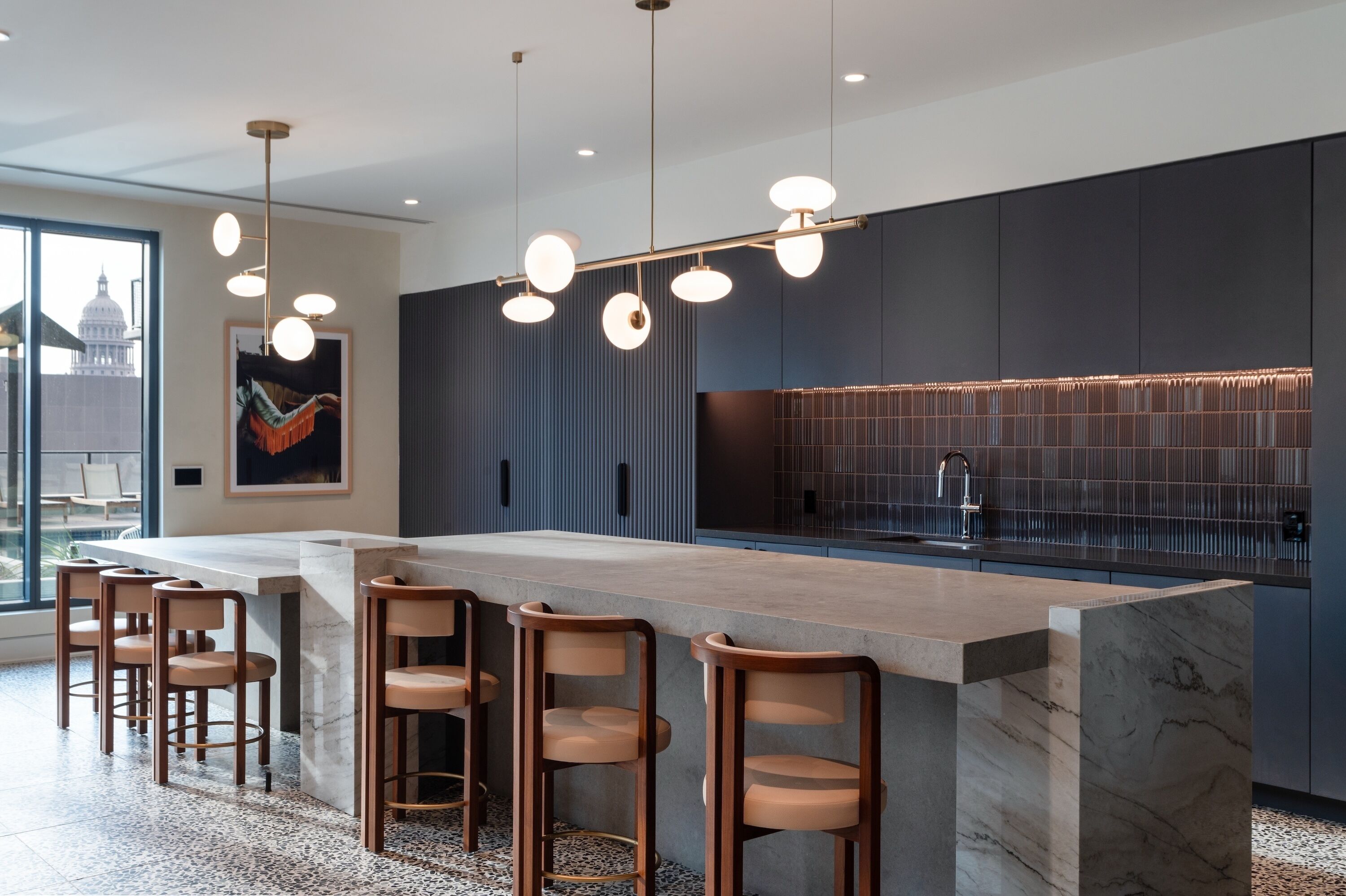 A modern kitchen with a marble island, bar stools, pendant lighting, and a cityscape view.