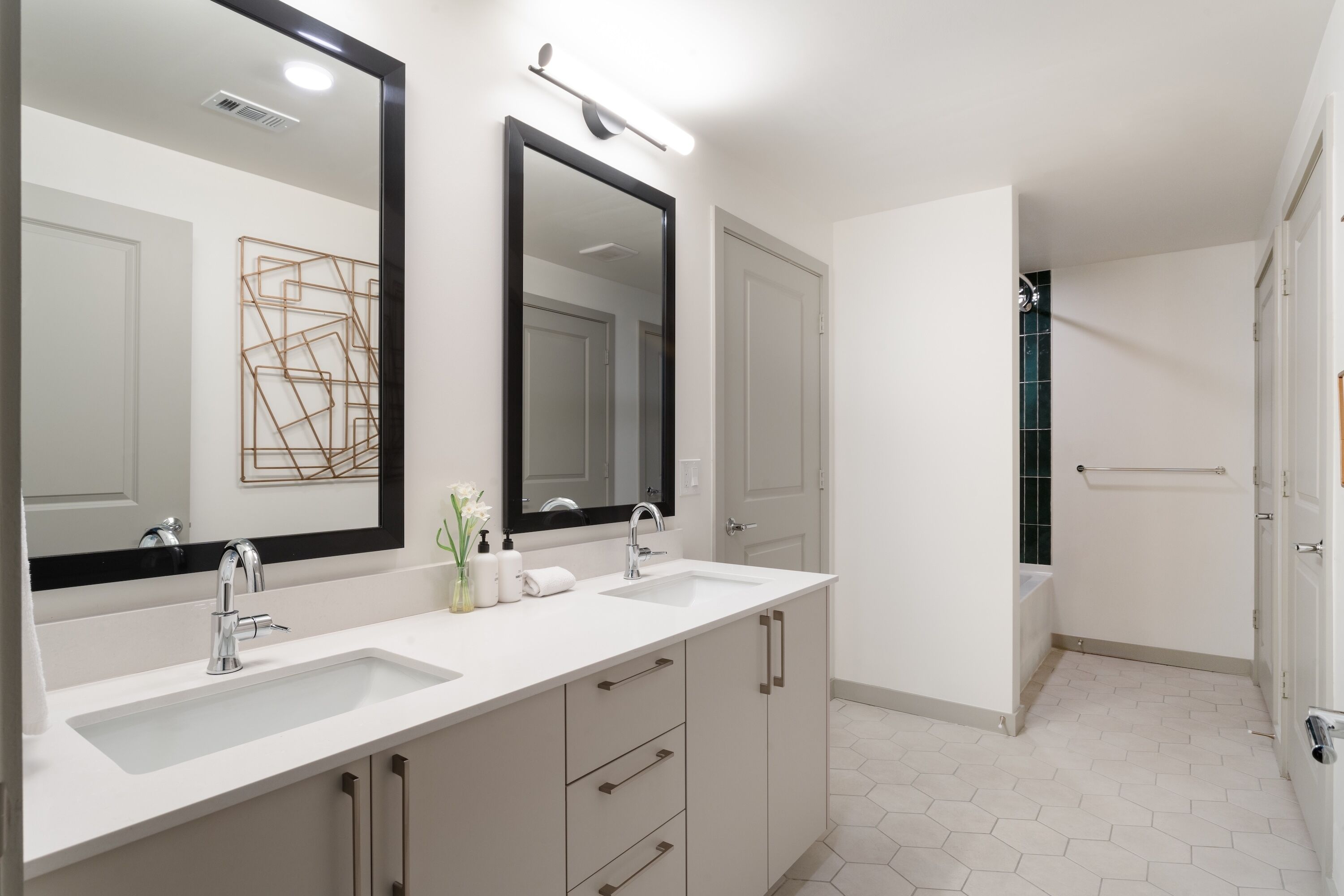 A modern bathroom with two sinks, a large mirror, and a walk-in shower.