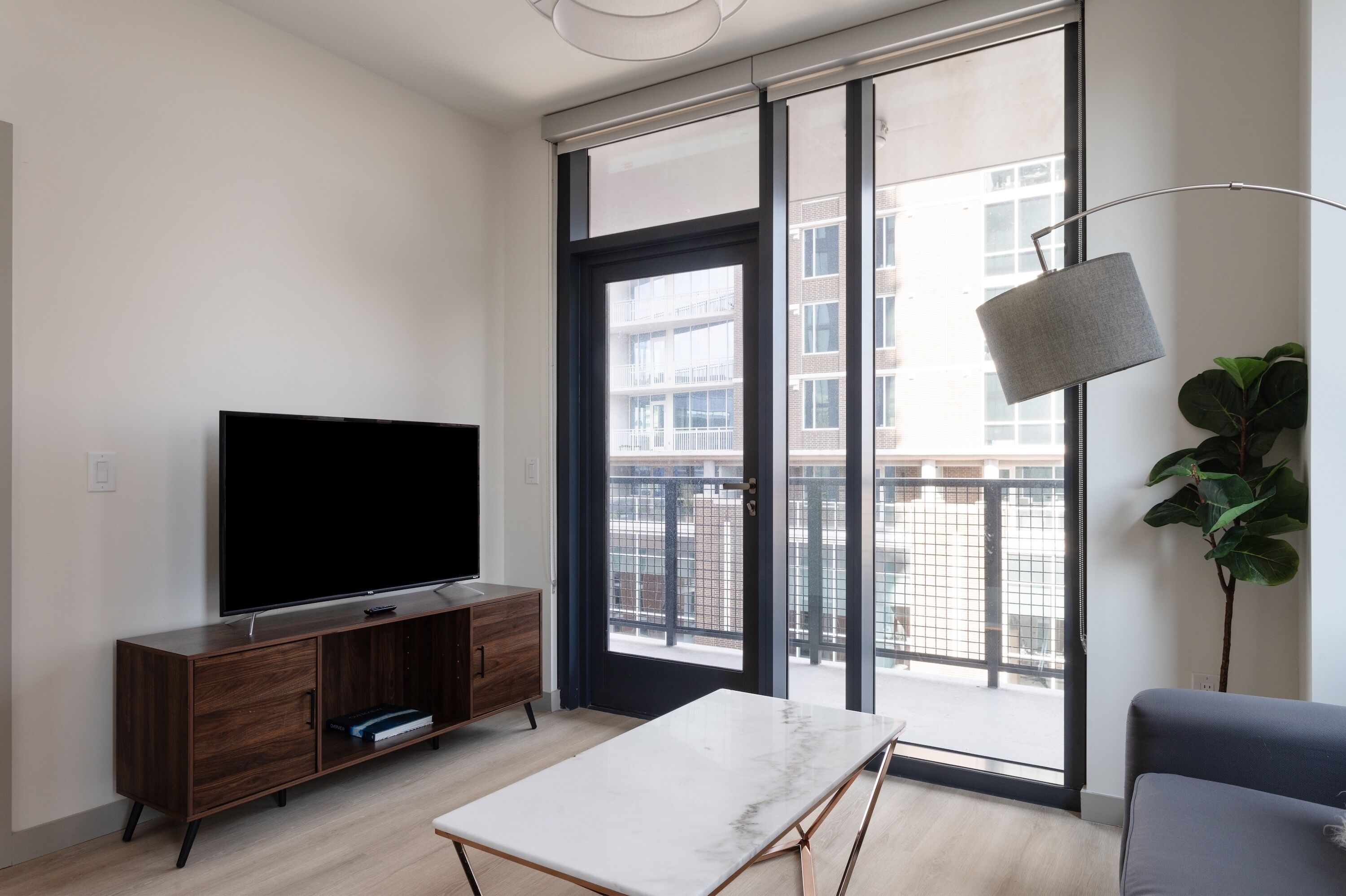 Una sala moderna con un televisor de pantalla plana, un mueble de madera y un ventanal con vistas a edificios.
