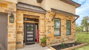 A stone building with a dark entrance door, a 'God Bless Texas' sign, and a small garden area with a potted plant. - Charming River Townhome A in Gruene (New Braunfels)