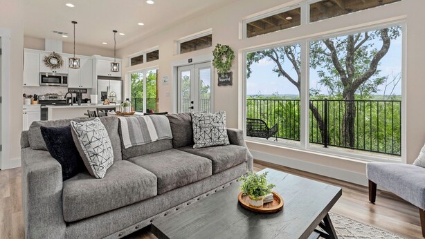 A modern living room with a grey sofa, a coffee table, and a view of a balcony with a tree. - Charming River Townhome A in Gruene (New Braunfels)