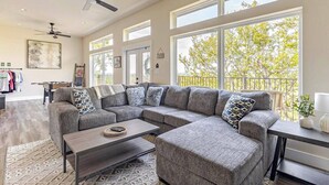 A spacious living room with a large sectional sofa, a coffee table, and a balcony with a railing. - Charming River Townhome A in Gruene (New Braunfels)