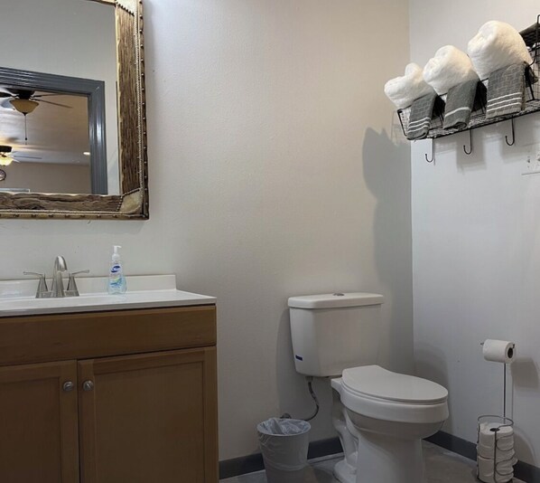 A bathroom with a white sink, a mirror, a toilet, and a shelf with towels.
