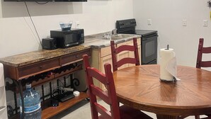 Une cuisine compacte équipée d’un four à micro-ondes, d’un grille-pain et d’une cuisinière. Une table à manger avec des chaises se trouve au premier plan.
