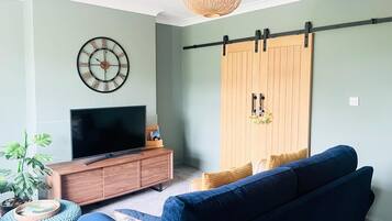 A living room with a TV, wooden cabinet, blue sofa, and a large wardrobe.