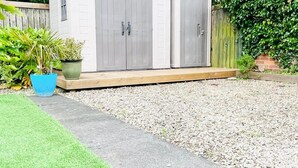 Un patio trasero con un sendero de grava, una terraza de madera y una planta en maceta.
