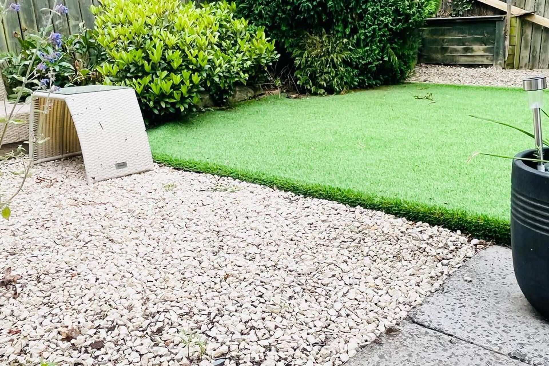 A garden with artificial grass, gravel, and a wooden fence.