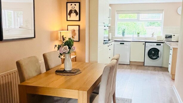 Cocina compacta con zona de comedor, que incluye una mesa con sillas, un florero con flores y una lavadora.