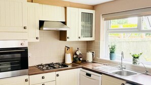Una cocina con armarios blancos, estufa, lavavajillas y ventana con vista a una cerca y plantas.