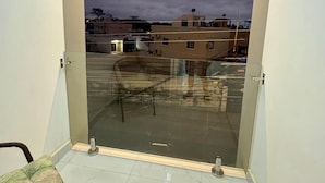 A balcony with a glass door, a chair, and a view of the surrounding buildings. - Hostal Las Orquideas 2 (Manta)
