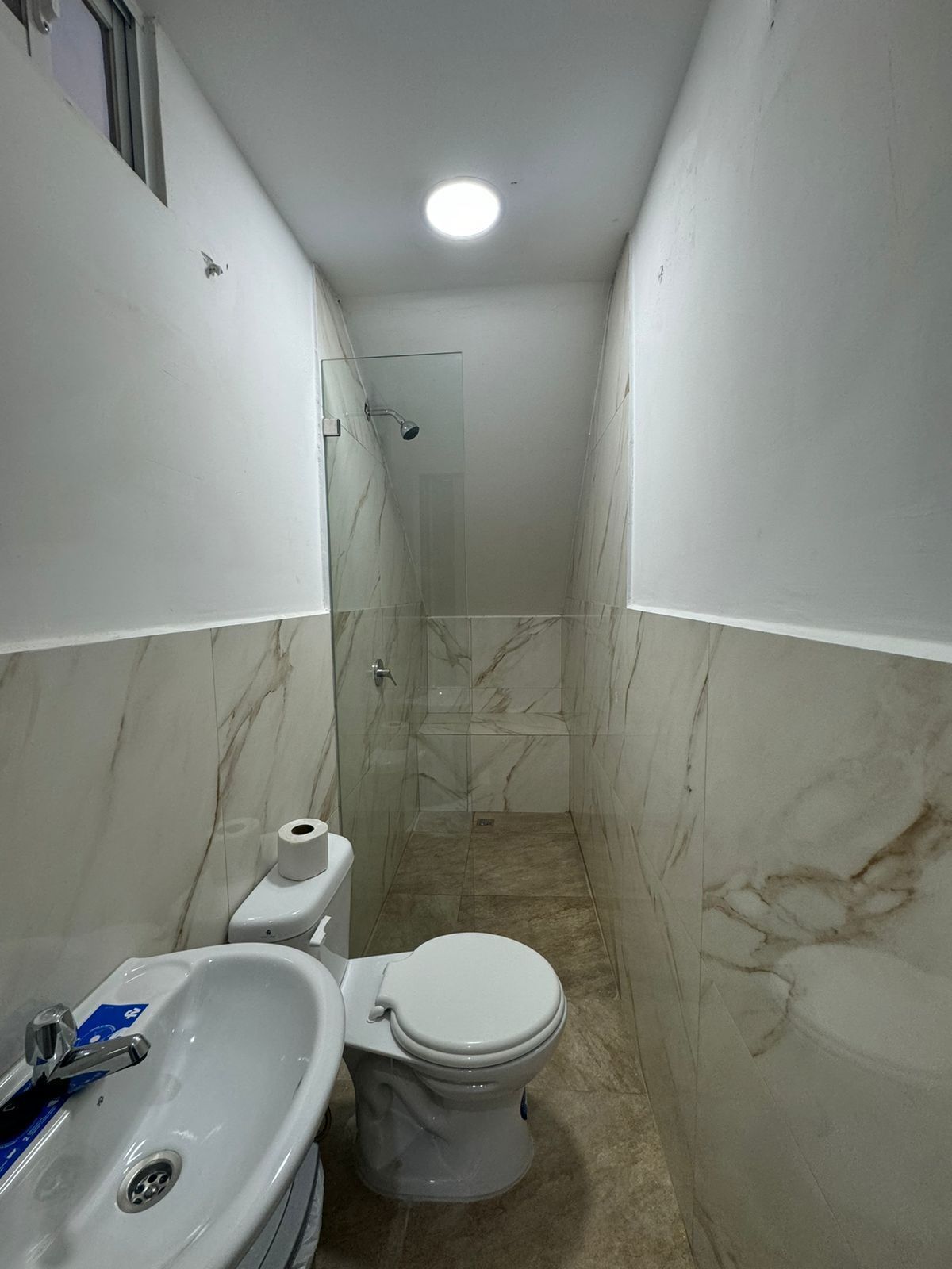 A narrow bathroom with a toilet, sink, and shower.