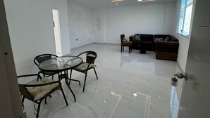 A modern living room with a dining area, featuring a glass-top table, wicker chairs, a black sofa, and a patterned ottoman. - Hostal Las Orquideas 2 (Manta)