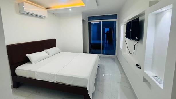 A modern bedroom with a bed, an air conditioning unit, a TV mounted on the wall, and a sliding glass door leading to a balcony. - Hostal Las Orquideas 2 (Manta)