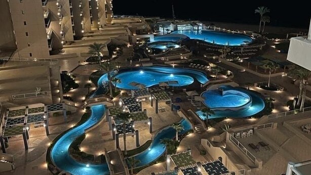 Un resort con varias piscinas, un edificio amplio con balcones y zonas de estar al aire libre.