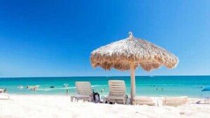 Una playa con una sombrilla de paja, arena blanca y agua cristalina azul.