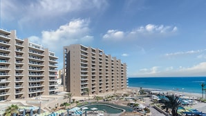 Un hotel con varias plantas, una zona de piscina y vistas a la playa.