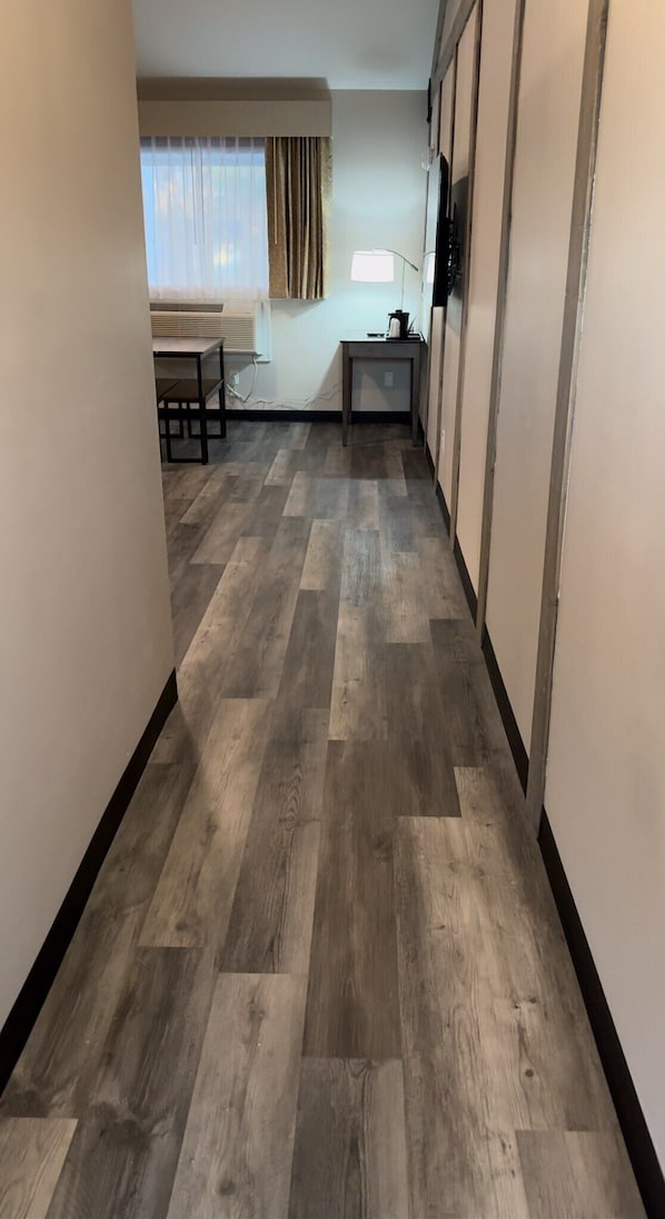 A hallway with a herringbone-patterned wooden floor, leading to a room with a window and curtains.