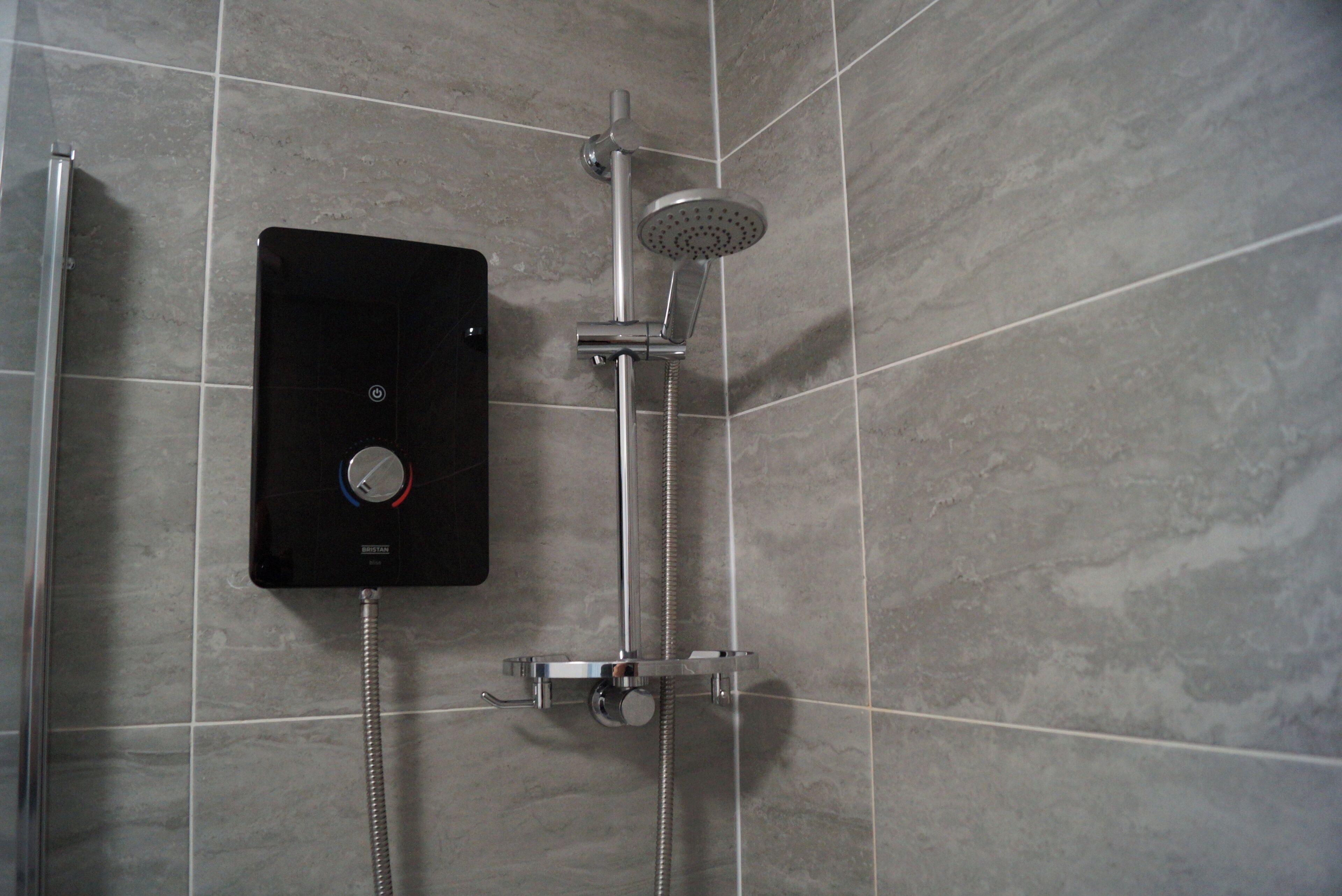 A modern bathroom with a built-in shower unit, a handheld showerhead, and a control panel.