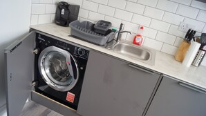 A compact kitchen with a built-in washer and dryer, a sink, and a coffee maker. - Bright & Stylish 1-bed Apt W/free Parking & Wi-fi (Dundee)