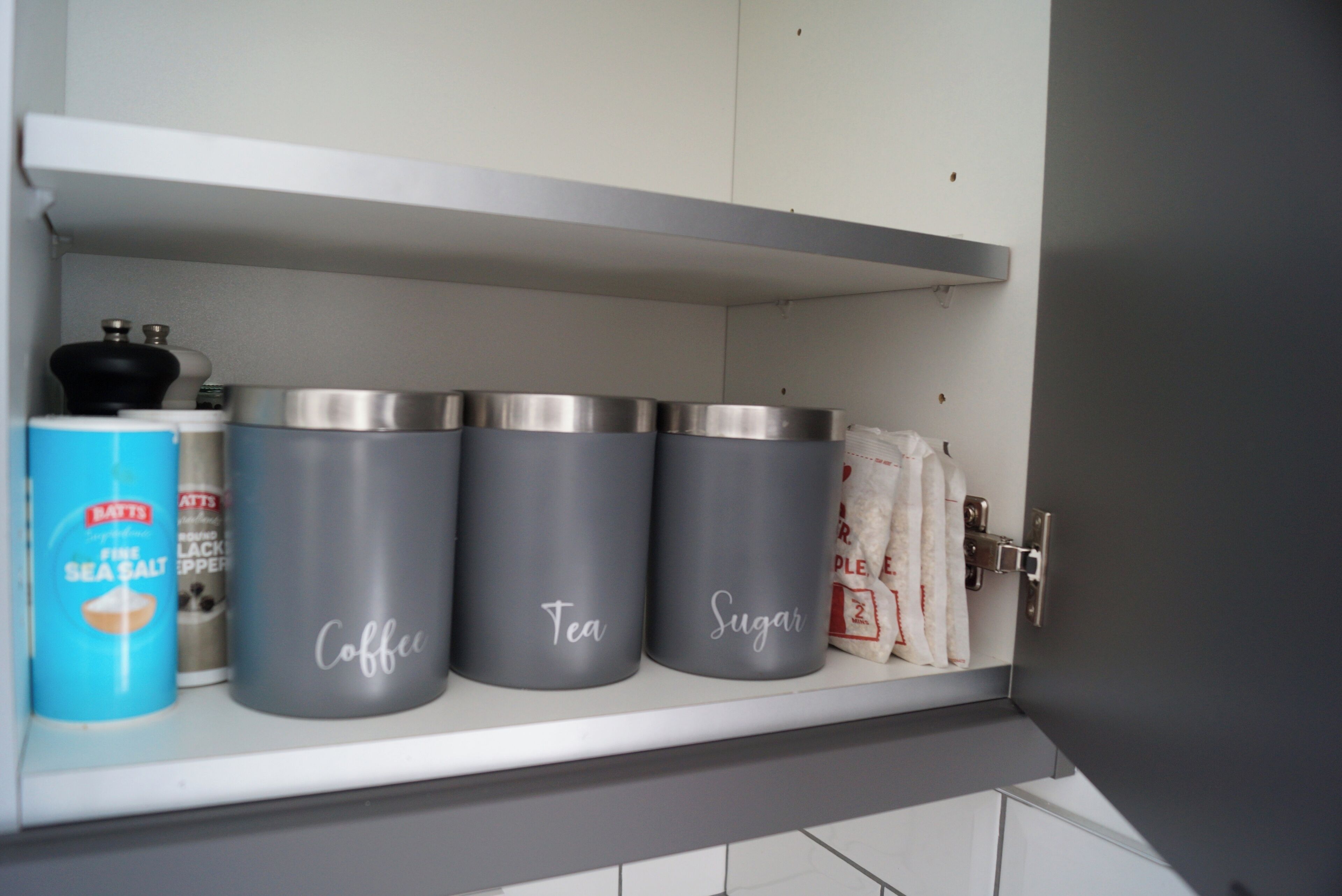 Ein Küchenregal mit beschrifteten Behältern für Kaffee, Tee und Zucker, sowie einem blauen Behälter für Meersalz.