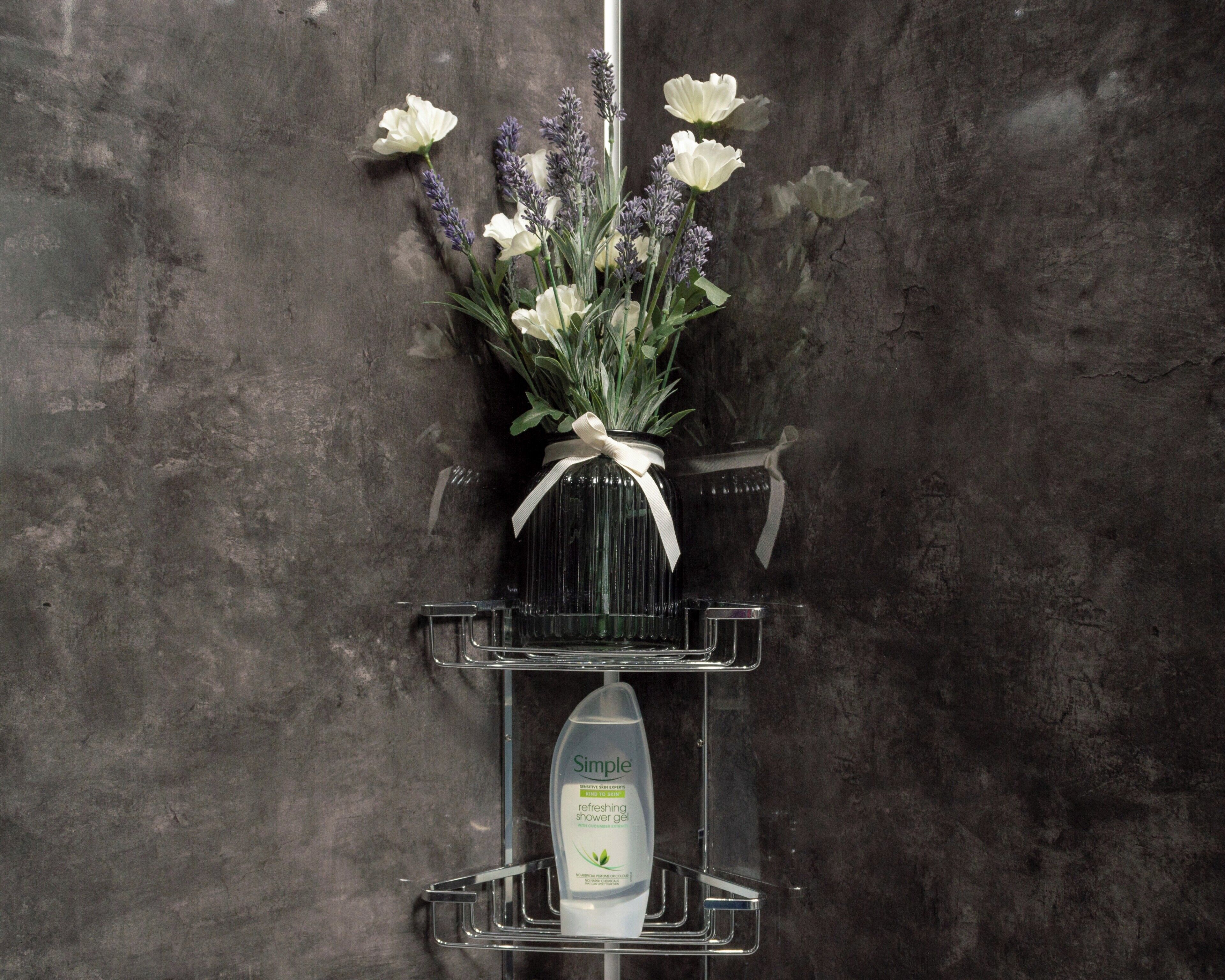 Une salle de bain avec un espace douche, une étagère en verre sur laquelle se trouve une bouteille de gel douche rafraîchissant de la marque Simple, et un vase avec des fleurs blanches et de la lavande.