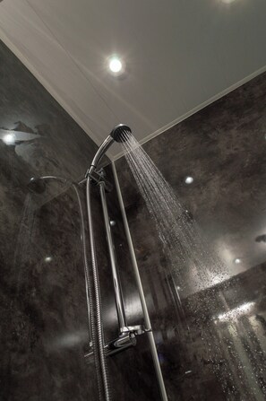 Un pommeau de douche laissant couler l’eau, fixé à un mur dont la surface est texturée.