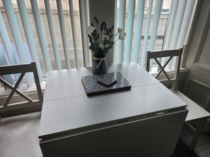 Une table blanche avec un ordinateur portable, un vase de fleurs et une chaise.
