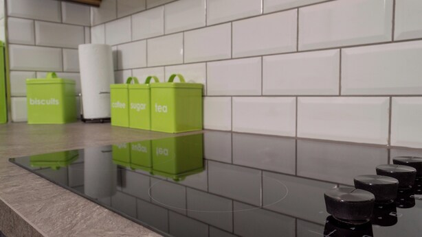 Eine Küche mit einer gefliesten Spritzschutzwand, einer glänzenden Arbeitsplatte und grünen Aufbewahrungsboxen, beschriftet mit Lebensmitteln.