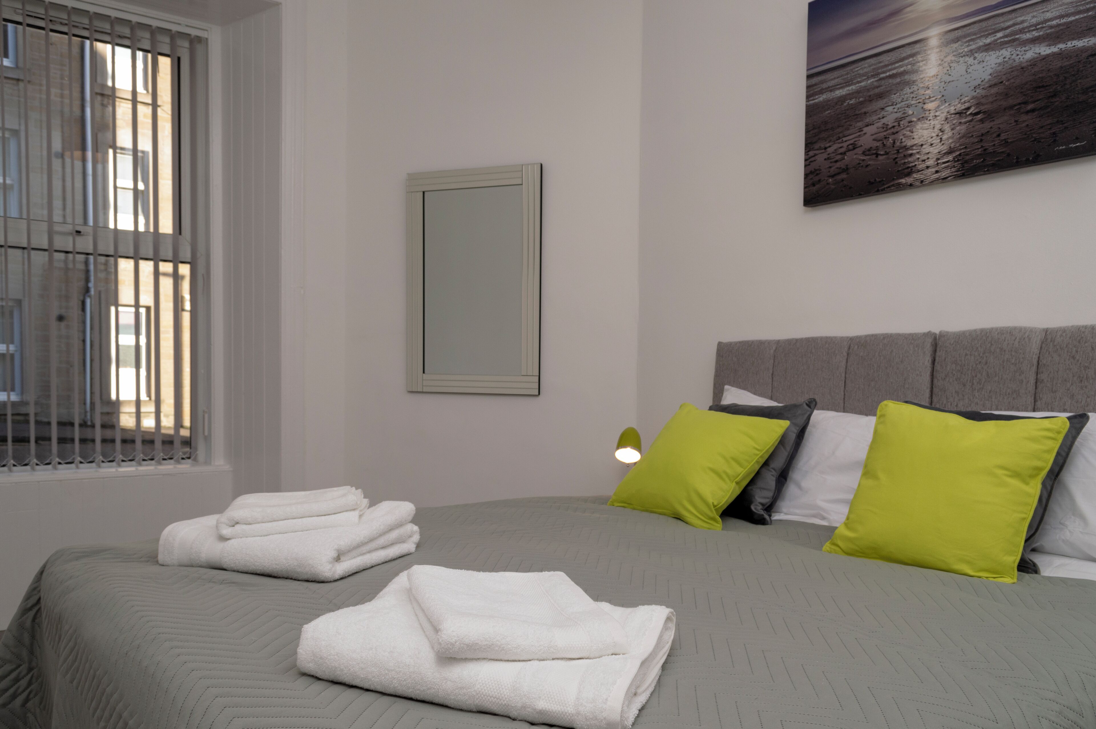 A neatly made bed with folded white towels, a grey headboard, and two green pillows.