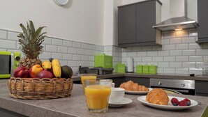 Eine Küchenarbeitsplatte mit Obstkorb, einem Glas Orangensaft, einem Teller mit Croissant und Beeren sowie einer Mikrowelle.