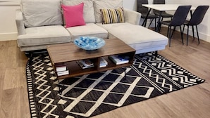 A living room with a sofa, a coffee table with books, a patterned rug, and a dining area with chairs and a table. - Batterseaflat/sleeps6/refurbished/tv (London)