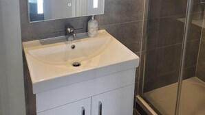 A bathroom with a white sink, a mirror, and a shower area. - Batterseaflat/sleeps6/refurbished/tv (London)