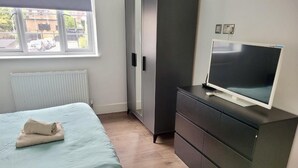 A bedroom with a bed, a TV on a dresser, a radiator, and a window with a view of the street. - Batterseaflat/sleeps6/refurbished/tv (London)