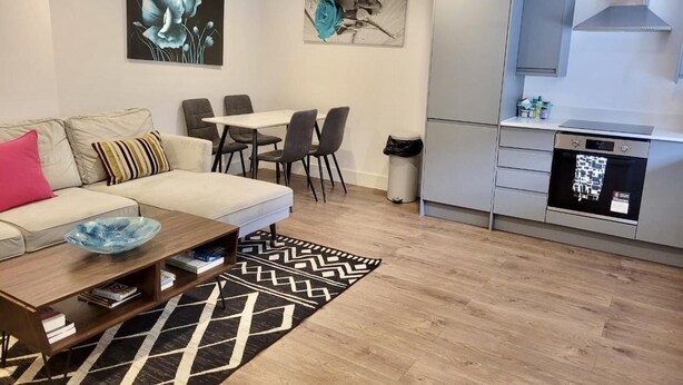 A modern living room with a sofa, coffee table, and a dining area with chairs. There is a kitchen with a dishwasher and cabinets. - Batterseaflat/sleeps6/refurbished/tv (London)