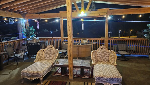 An outdoor covered patio with two ornate chairs, a table, and a grill.