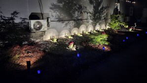 A garden with a white wall, string lights, and a fan.