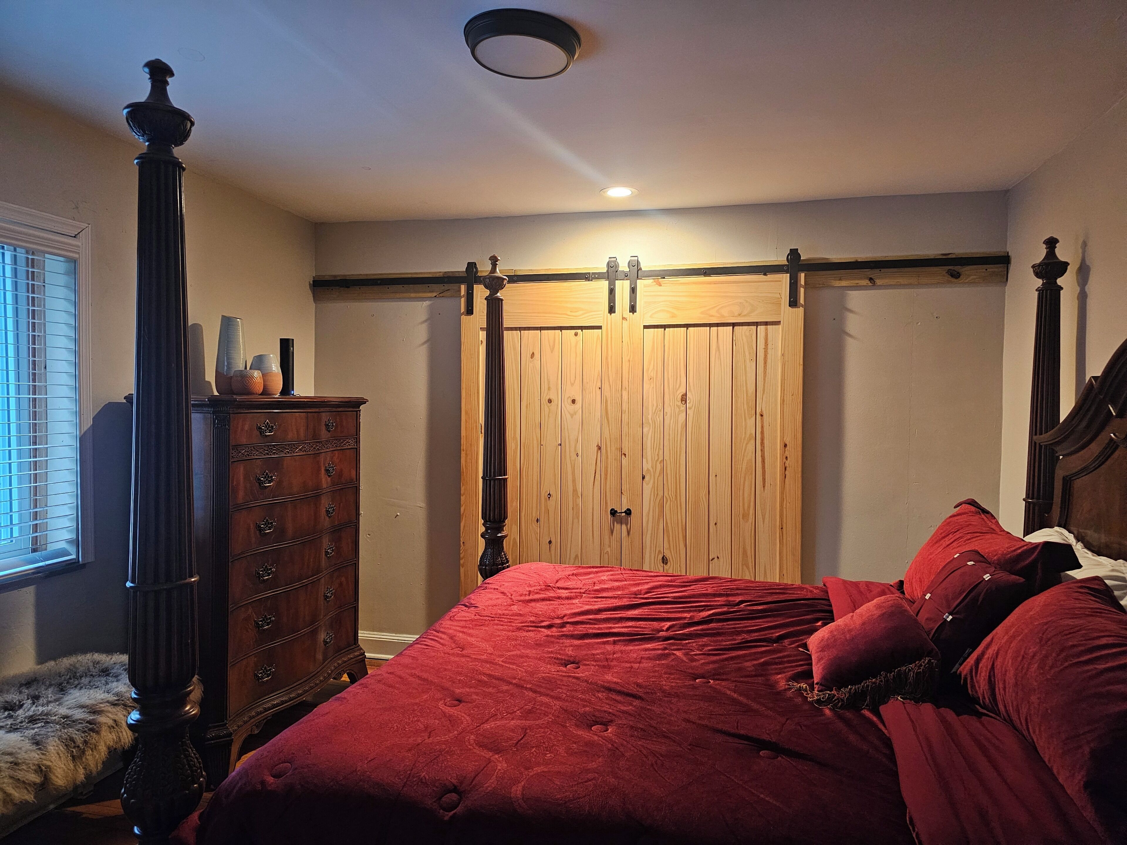 Un dormitorio con un armario de madera, una cama con ropa de cama roja y un aparador con adornos.