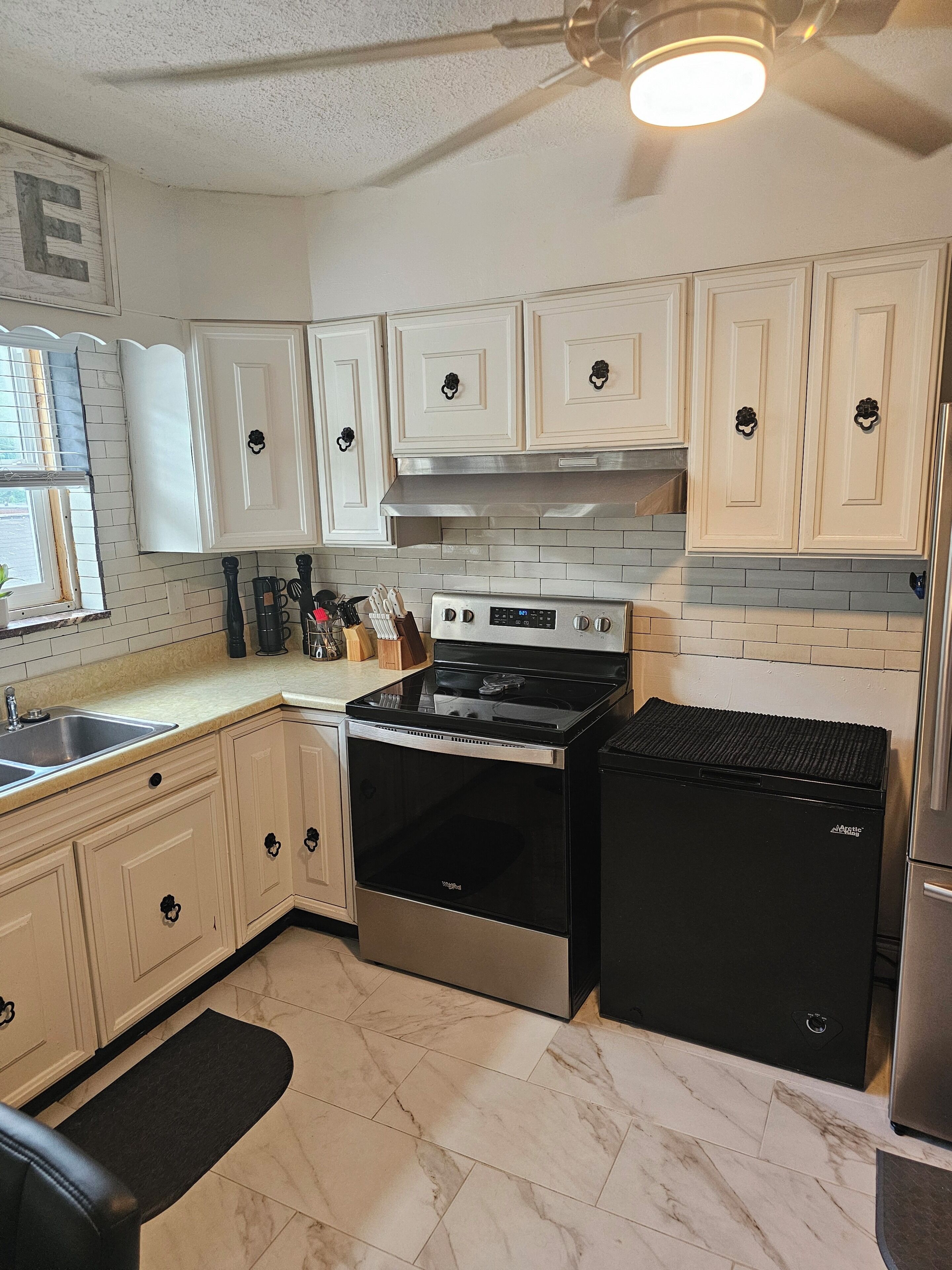 Una cocina con armarios blancos, una estufa negra y un refrigerador.