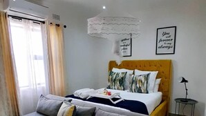 A modern bedroom with a sofa bed, a bed with a yellow headboard, and a small bedside table. - Sunset Bliss Paradise in Lilongwe (Lilongwe)