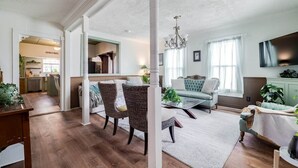 A spacious living area with a dining table, wicker chairs, a sofa, and a television. - Historic Colonial Retreat in Downtown Brunswick (Brunswick)