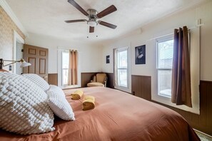 A bedroom with a bed, a ceiling fan, a window with curtains, and a chair.