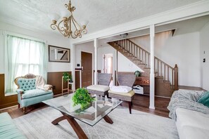 A spacious living room with a glass coffee table, a blue armchair, and a staircase leading to another level. - Historic Colonial Retreat in Downtown Brunswick (Brunswick)