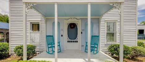 A two-story house with a porch, a front door, and two green chairs.